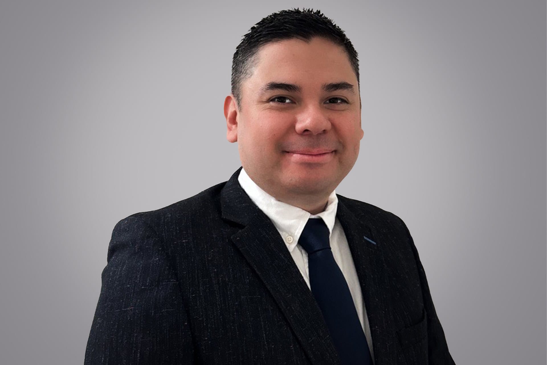 Cristian in a suit smiling at the camera against a grey background