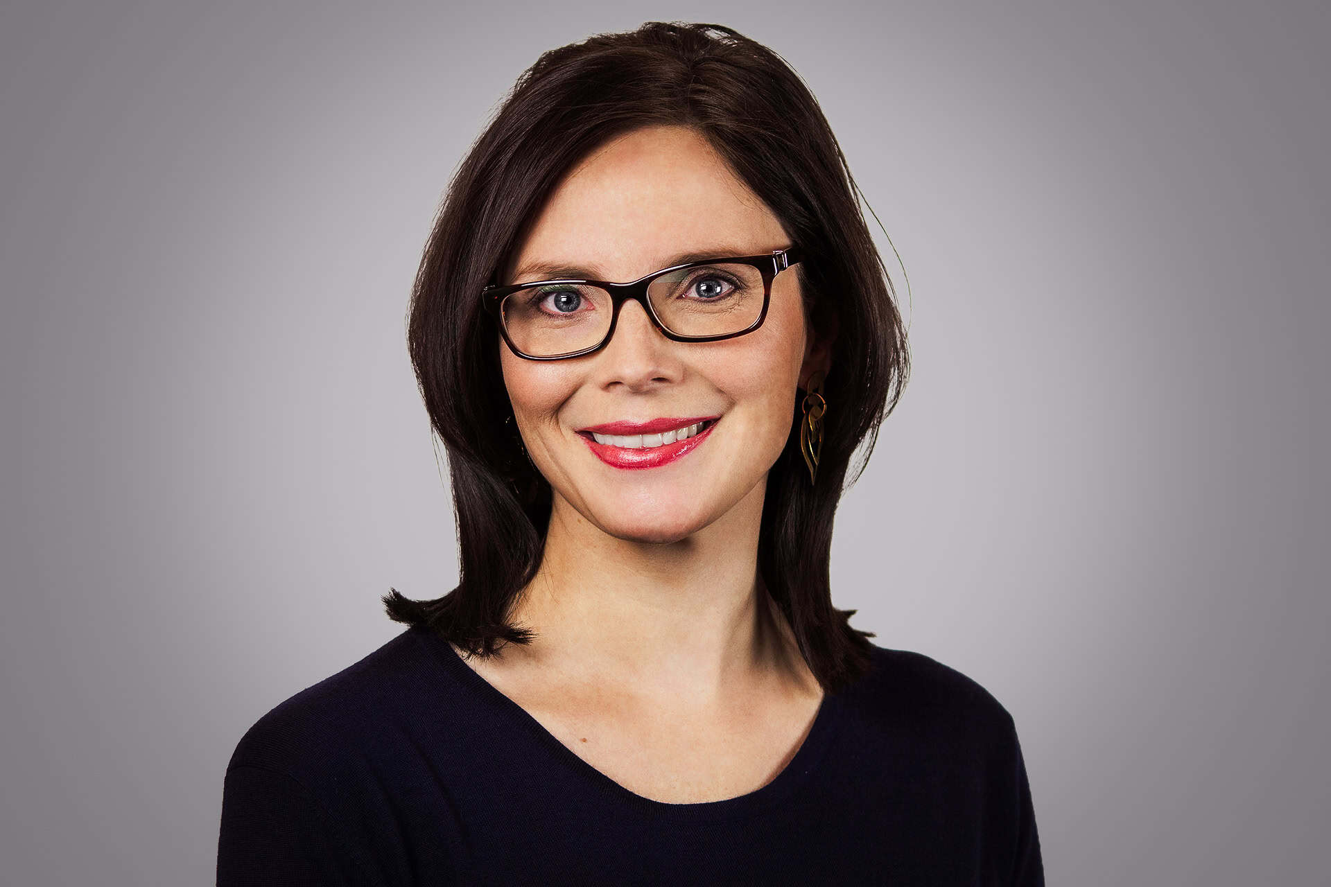 Courtney smiles at the camera, wearing a navy shirt, against a grey background.