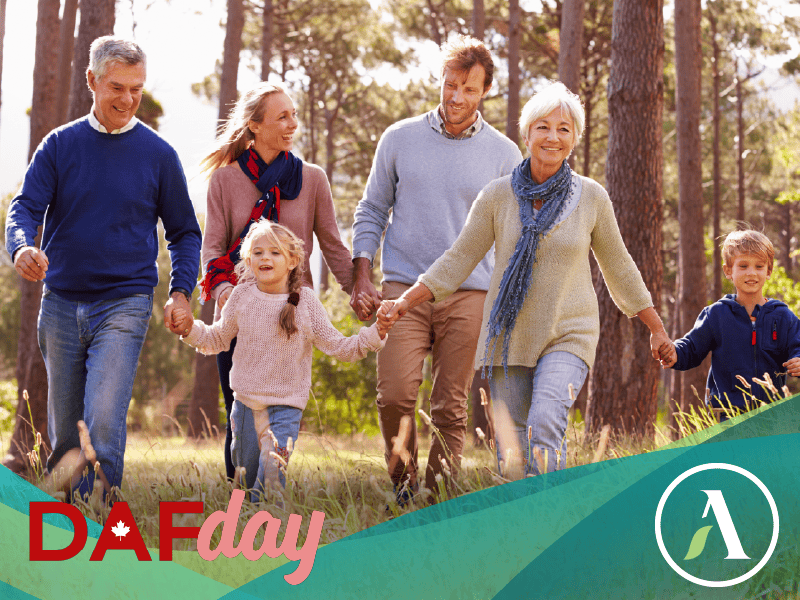 A multigenerational family walks through the autumn woods together, smiling and holding hands.