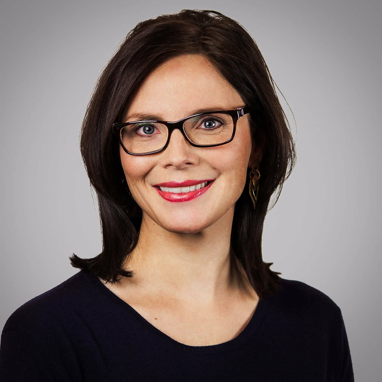Courtney smiles at the camera, wearing a navy shirt, against a grey background.